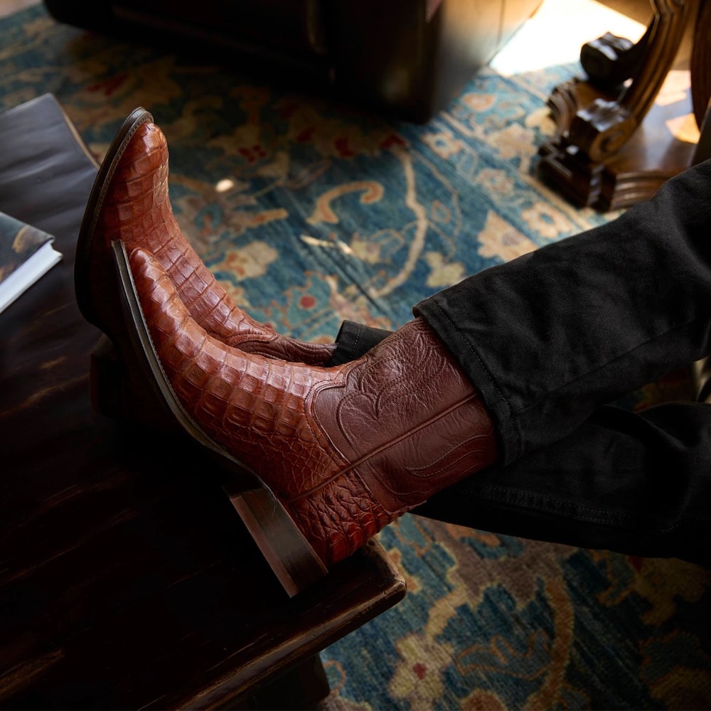 Presenta un par de botas Tremaine Caiman de 12" en color marrón en el modelo.